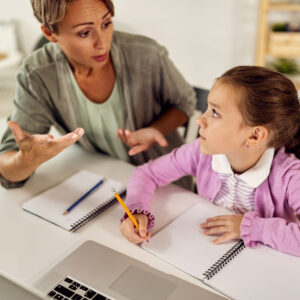 Small girl learning at home and listening to her mother who is assisting her with a homework.